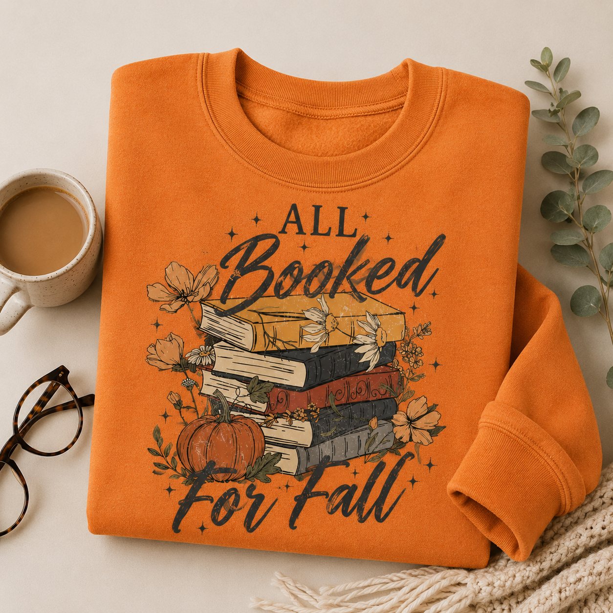 Folded Tangerine Fall Book Lover Sweatshirt with All Booked for Fall books and pumpkin graphic, styled with coffee, reading glasses and a cozy blanket.