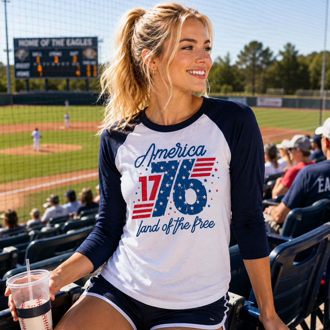 Woman wearing a 'America 1776 Land of the Free' shirt at a baseball game.