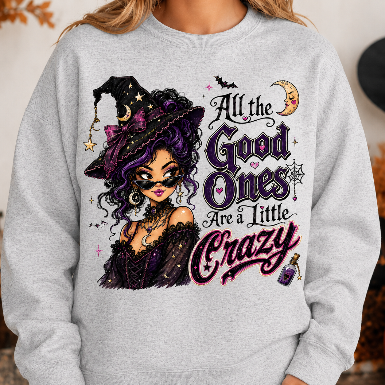 Ash Gray Halloween witch sweatshirt modeled with the “All the Good Ones Are a Little Crazy” graphic, featuring a purple-haired witch, crescent moon, bats, spiderweb, stars, and potion details.
