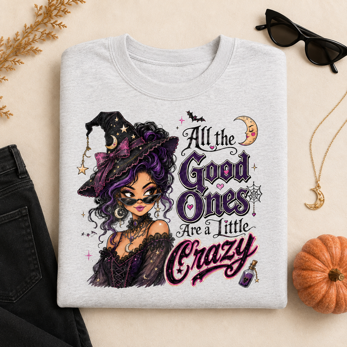 Ash Gray Halloween witch sweatshirt laid flat with the “All the Good Ones Are a Little Crazy” graphic, styled with black jeans, sunglasses, a crescent moon necklace, pumpkin, and autumn accents.
