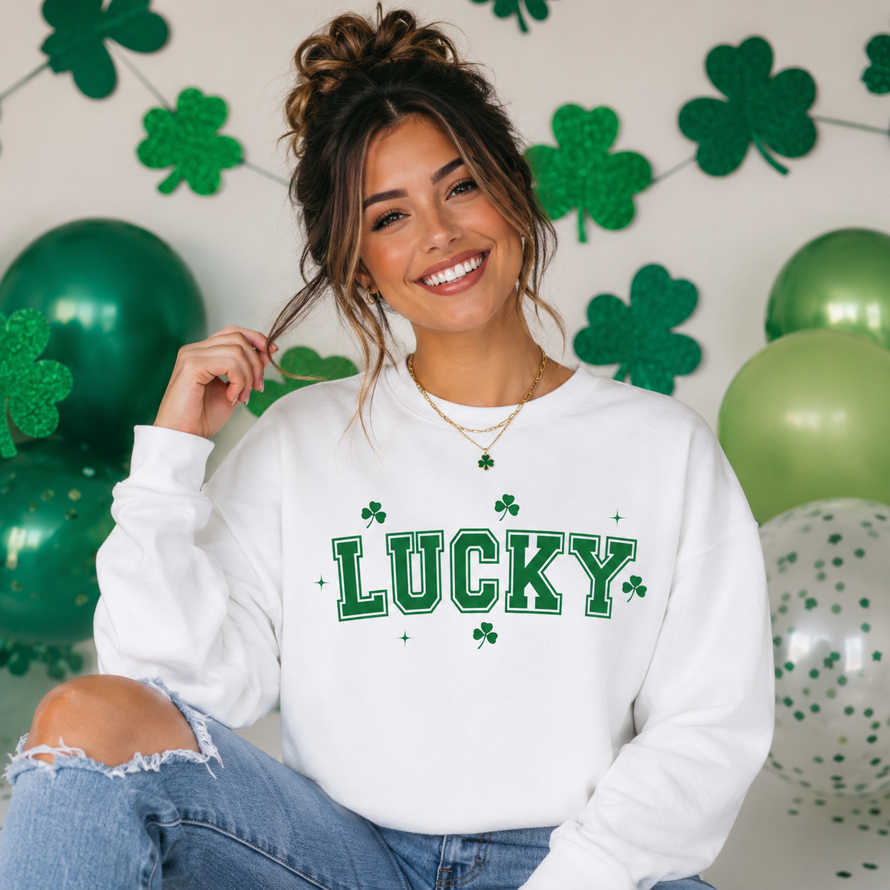 Woman wearing a white sweatshirt with 'LUCKY' and shamrock design, sitting in front of green balloons and shamrock decorations.