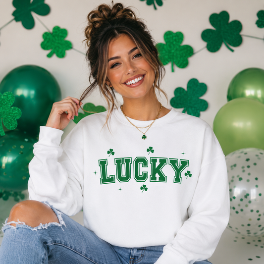 Woman wearing a white sweatshirt with 'LUCKY' and shamrock design, sitting in front of green balloons and shamrock decorations.