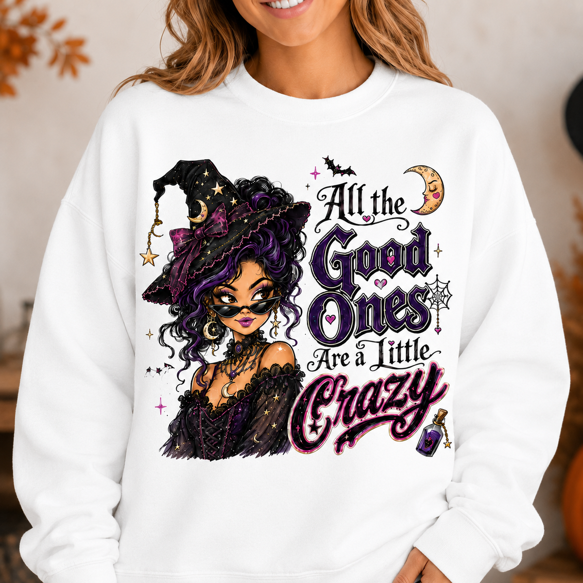 White Halloween witch sweatshirt modeled with the “All the Good Ones Are a Little Crazy” graphic, featuring a purple-haired witch, crescent moon, bats, stars, spiderweb, and potion details.
