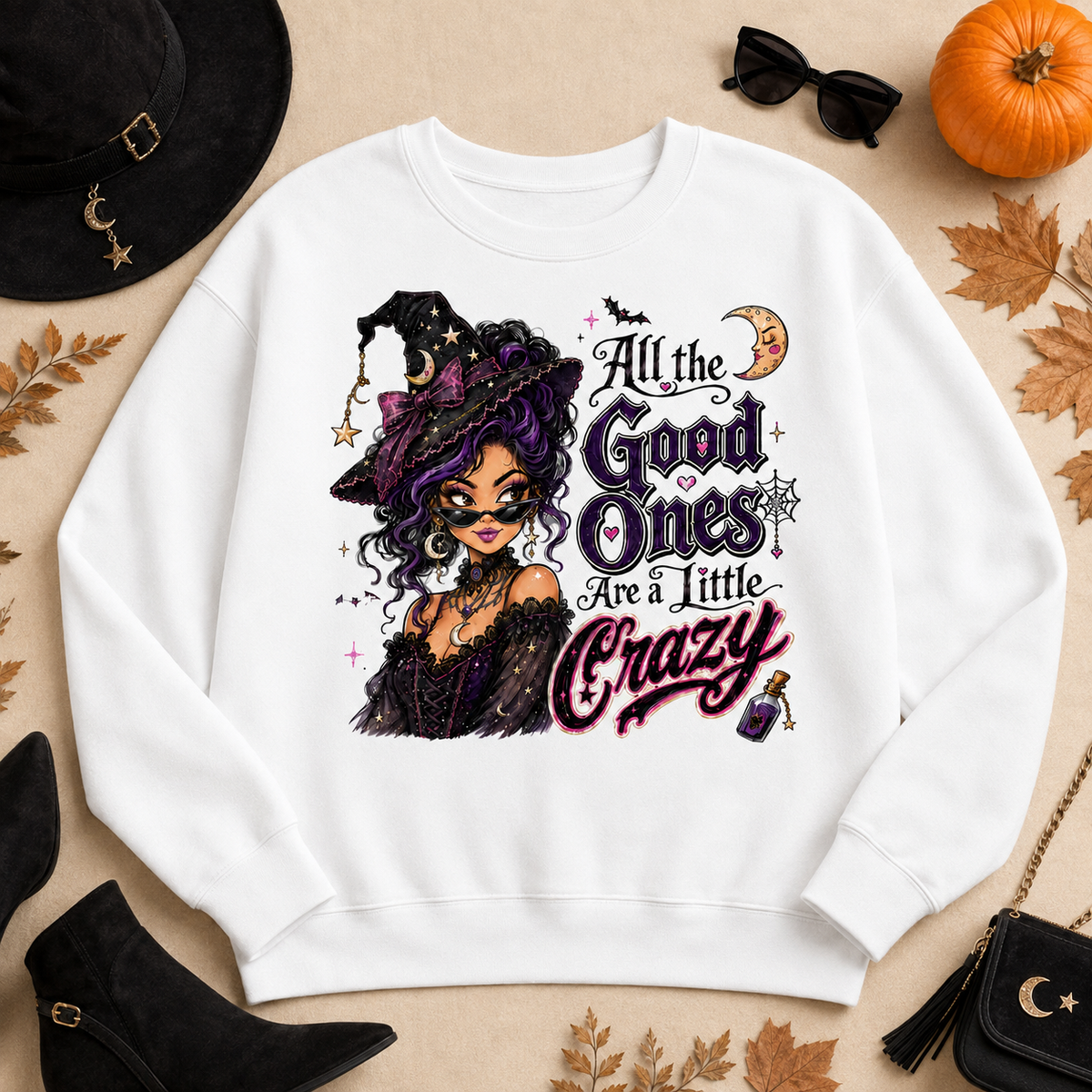 White Halloween witch sweatshirt laid flat with the “All the Good Ones Are a Little Crazy” graphic, styled with a witch hat, pumpkin, autumn leaves, sunglasses, boots, and Halloween accessories.
