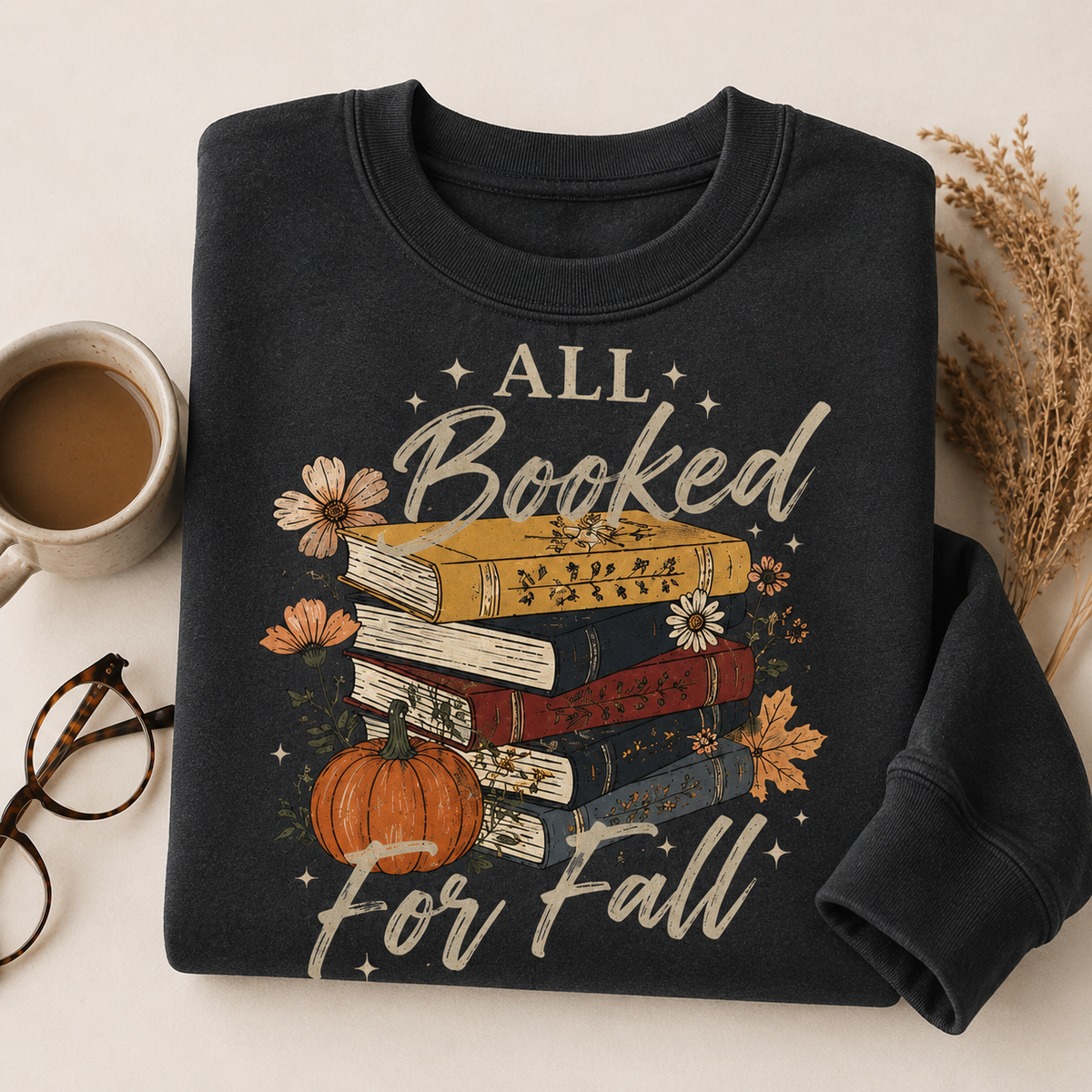 Folded Heather Black Fall Book Lover Sweatshirt with All Booked for Fall books and pumpkin graphic, styled with coffee and reading glasses.