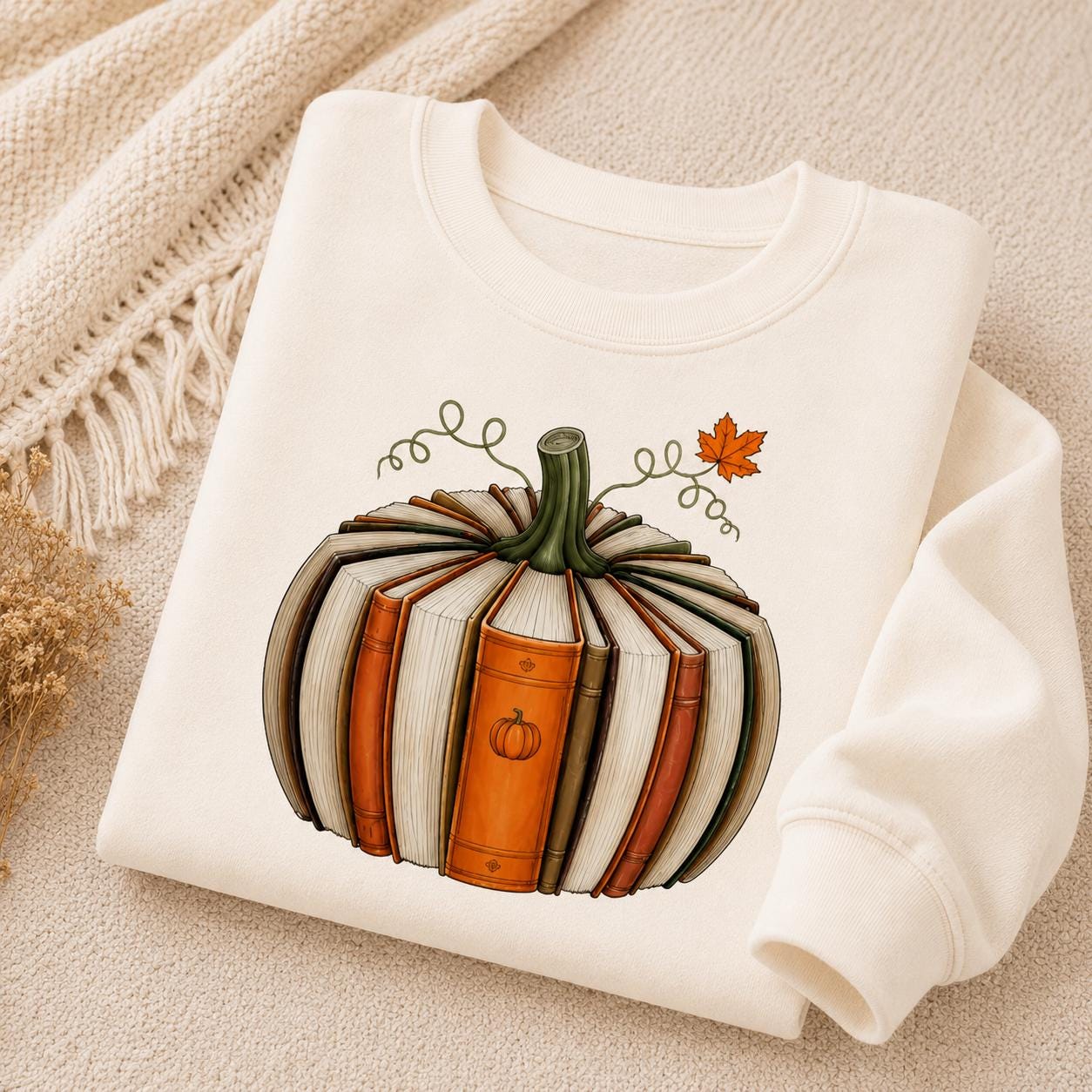 Folded off-white Fall Book Lover Sweatshirt with pumpkin-shaped book graphic in a cozy autumn setting
