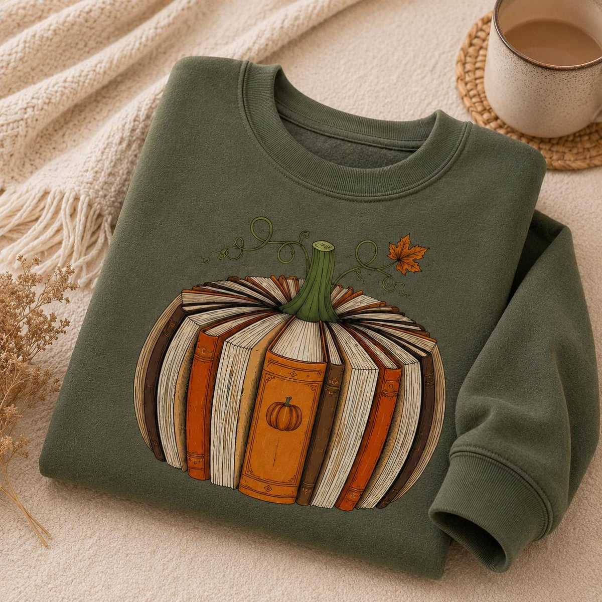 Folded military green Fall Book Lover Sweatshirt with pumpkin-shaped book graphic in a cozy autumn setting with coffee and knit blanket
