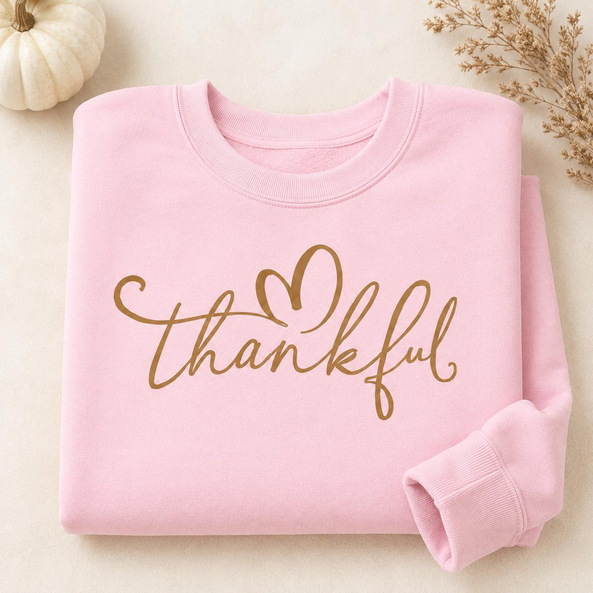Folded pink Thankful Sweatshirt with gold script heart design and fall pumpkin accents
