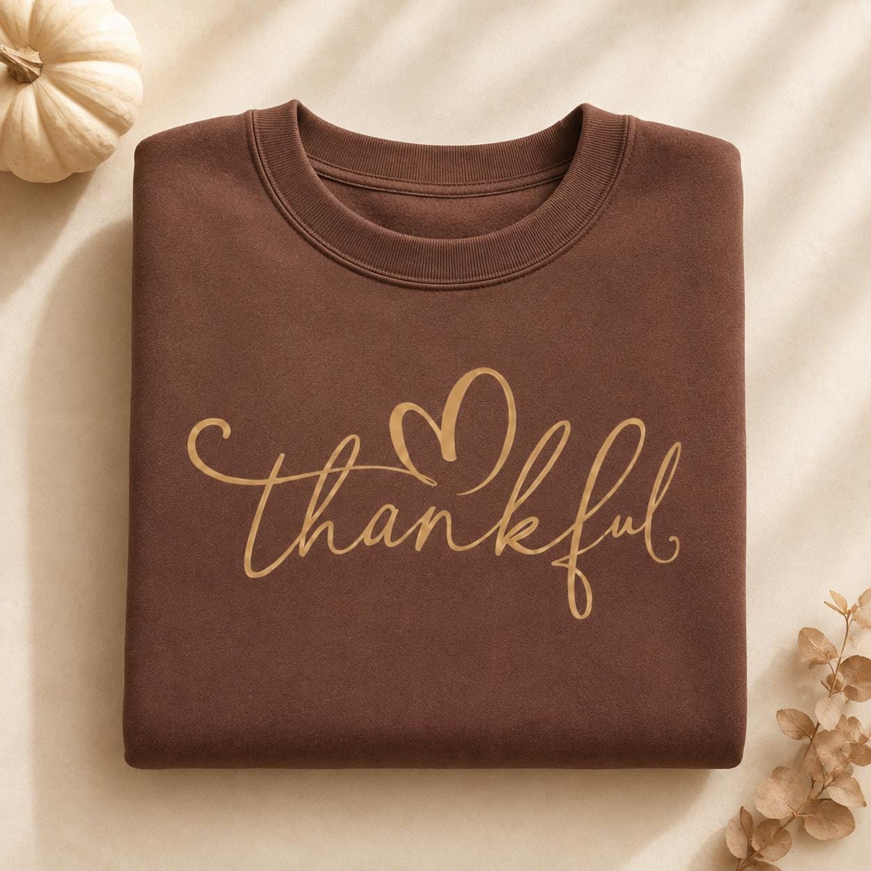 Folded brown Thankful Sweatshirt with gold script heart design and fall pumpkin accents
