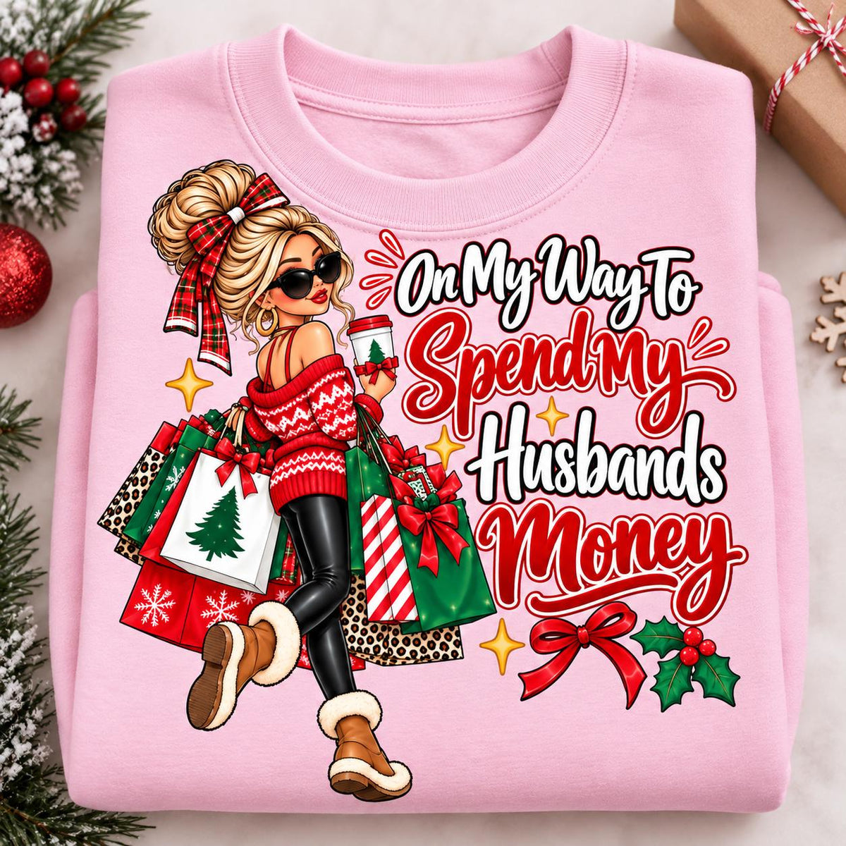 Folded light pink holiday shopping sweatshirt with festive woman and gift bags.