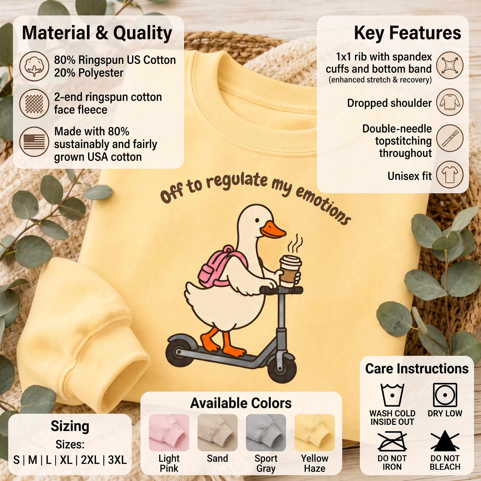 A pale yellow children's sweatshirt laid flat on a woven mat with decorative greenery. The sweatshirt has a cartoon duck riding a scooter with the phrase 'Off to regulate my emotions' across the chest.