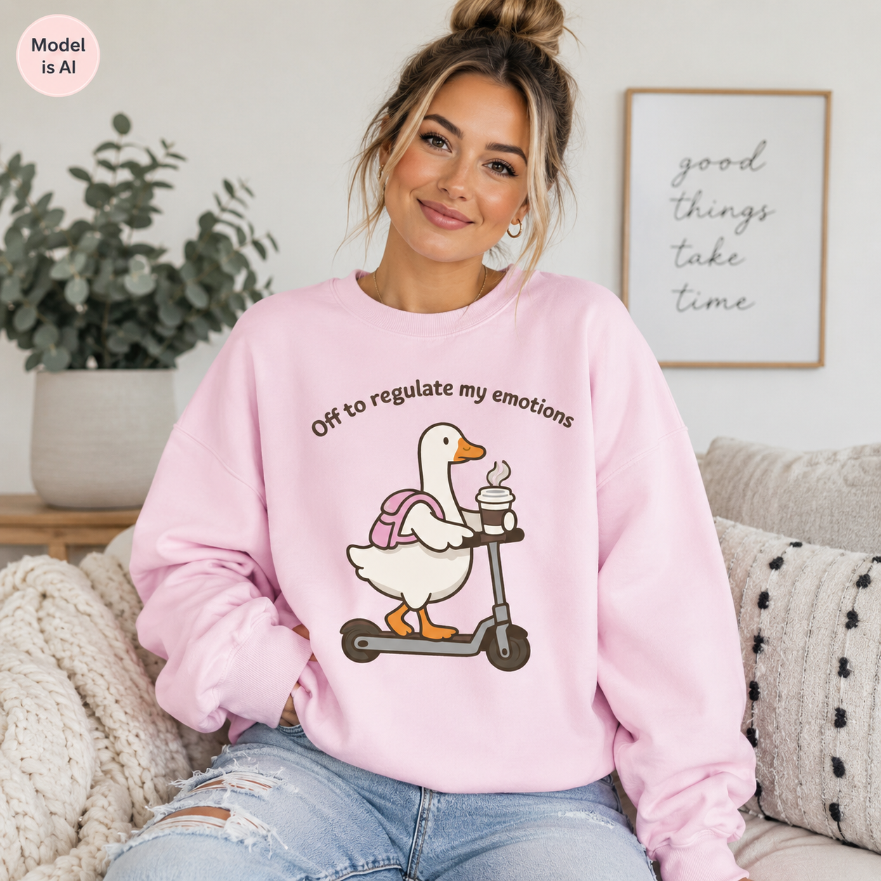 A woman sitting on a couch wearing a light pink sweatshirt with a graphic of a white goose on a scooter and the text 'Off to regulate my emotions'.