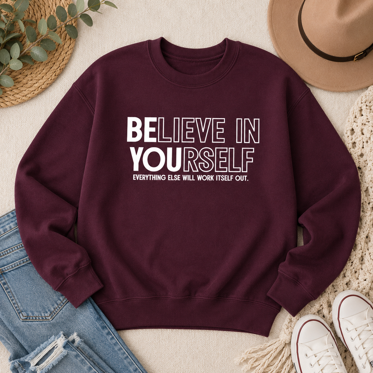 A maroon crewneck sweatshirt with the motivational text 'BELIEVE IN YOURSELF' and 'EVERYTHING ELSE WILL WORK ITSELF OUT.' printed in white on the front.