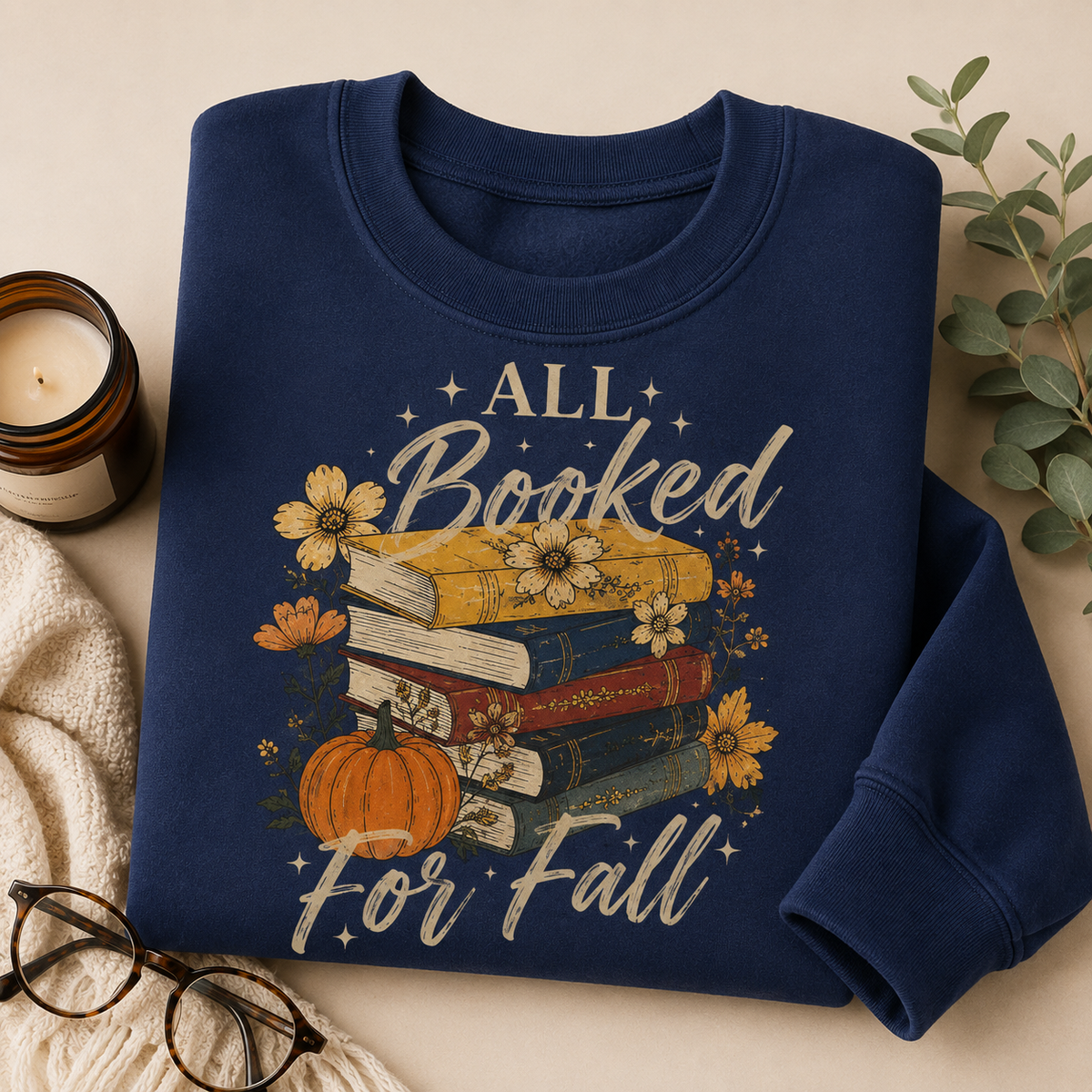 Folded Navy Fall Book Lover Sweatshirt with All Booked for Fall books and pumpkin graphic, styled with a candle, reading glasses and cozy blanket.