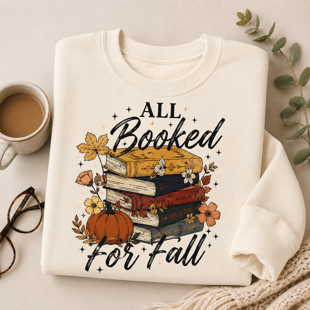 Folded Off White Fall Book Lover Sweatshirt with All Booked for Fall books and pumpkin graphic, styled with coffee, reading glasses and a cozy blanket.