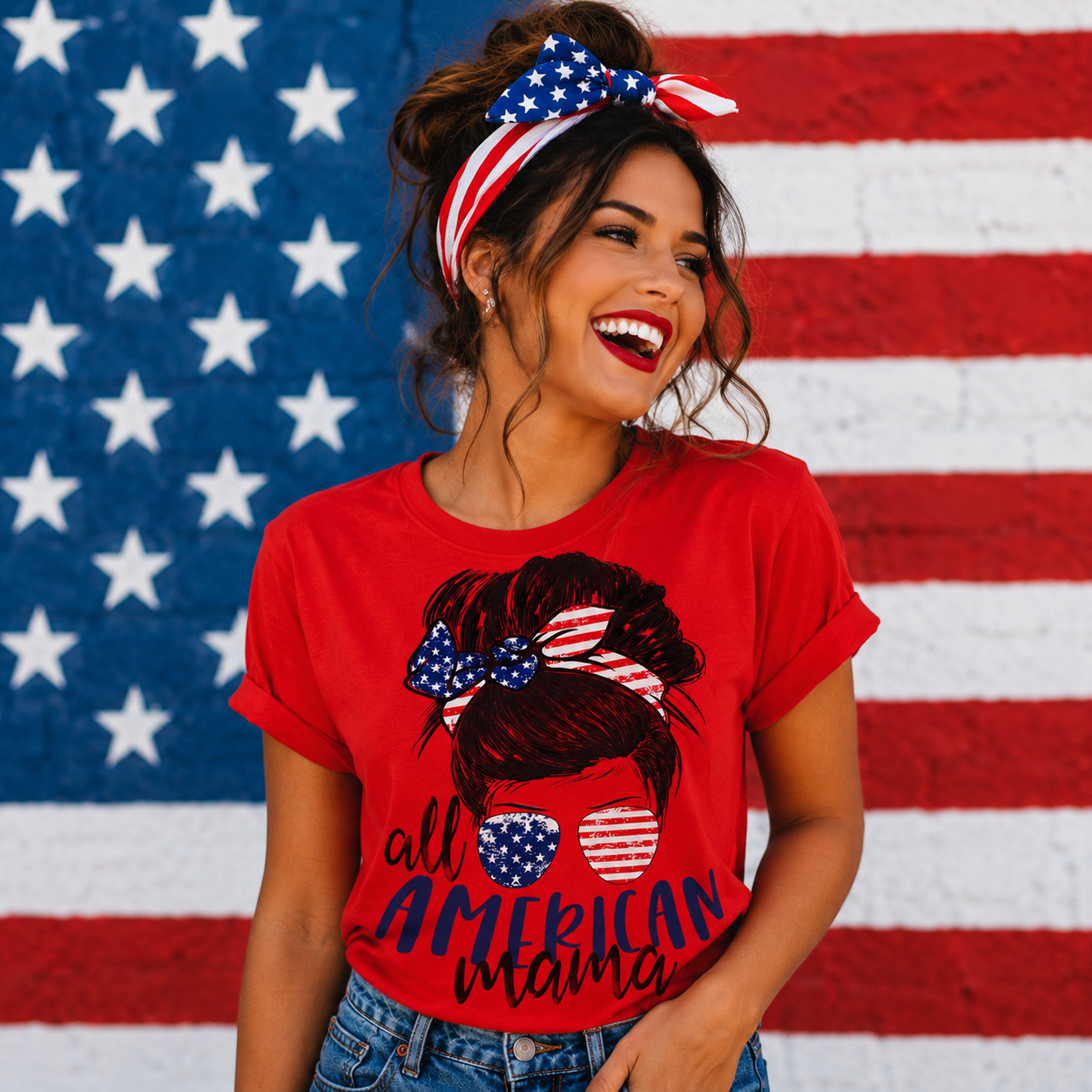 Woman wearing a red 'All American Mama' t-shirt with an American flag headband and sunglasses graphic, standing in front of an American flag.