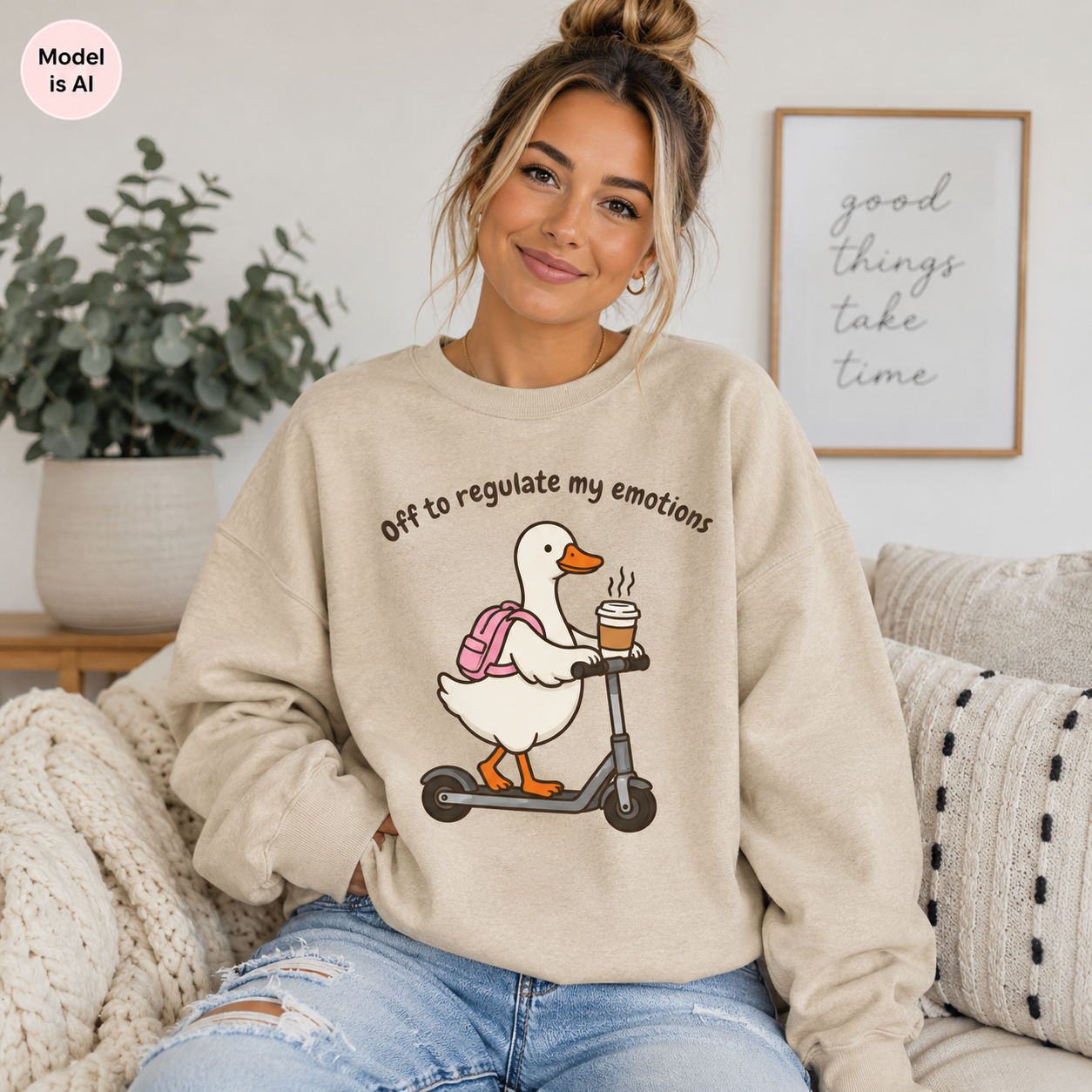 A woman sitting on a couch wearing a beige crewneck sweatshirt with a cartoon duck riding a scooter and the text 'Off to regulate my emotions'.