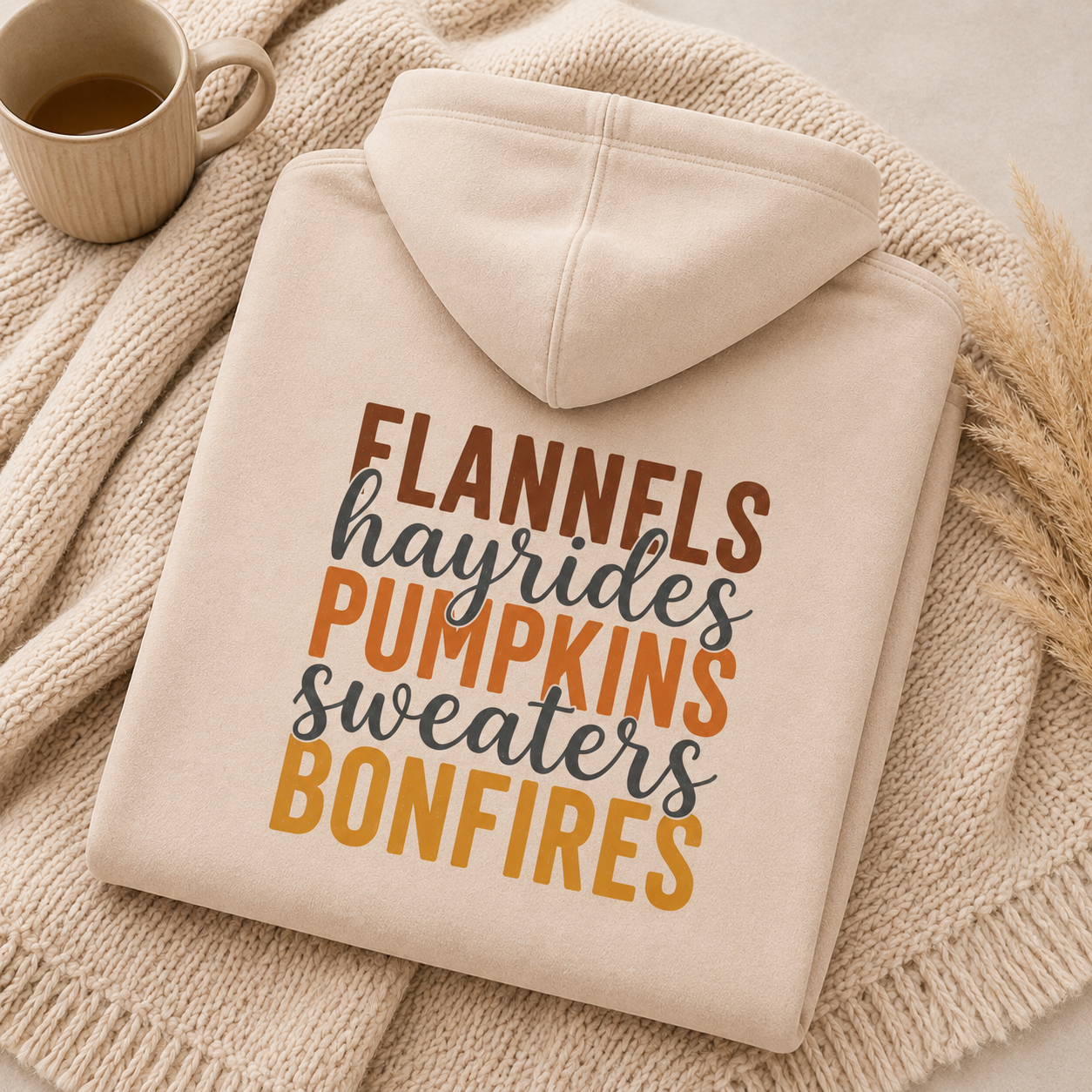 Folded Sand fall hoodie with Flannels, Hayrides, Pumpkins, Sweaters and Bonfires graphic printed on the back.