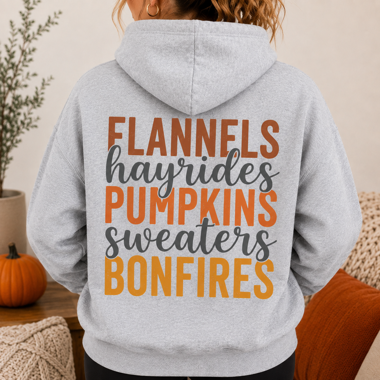 Woman wearing a Sport Gray fall hoodie with Flannels, Hayrides, Pumpkins, Sweaters and Bonfires graphic printed on the back.
