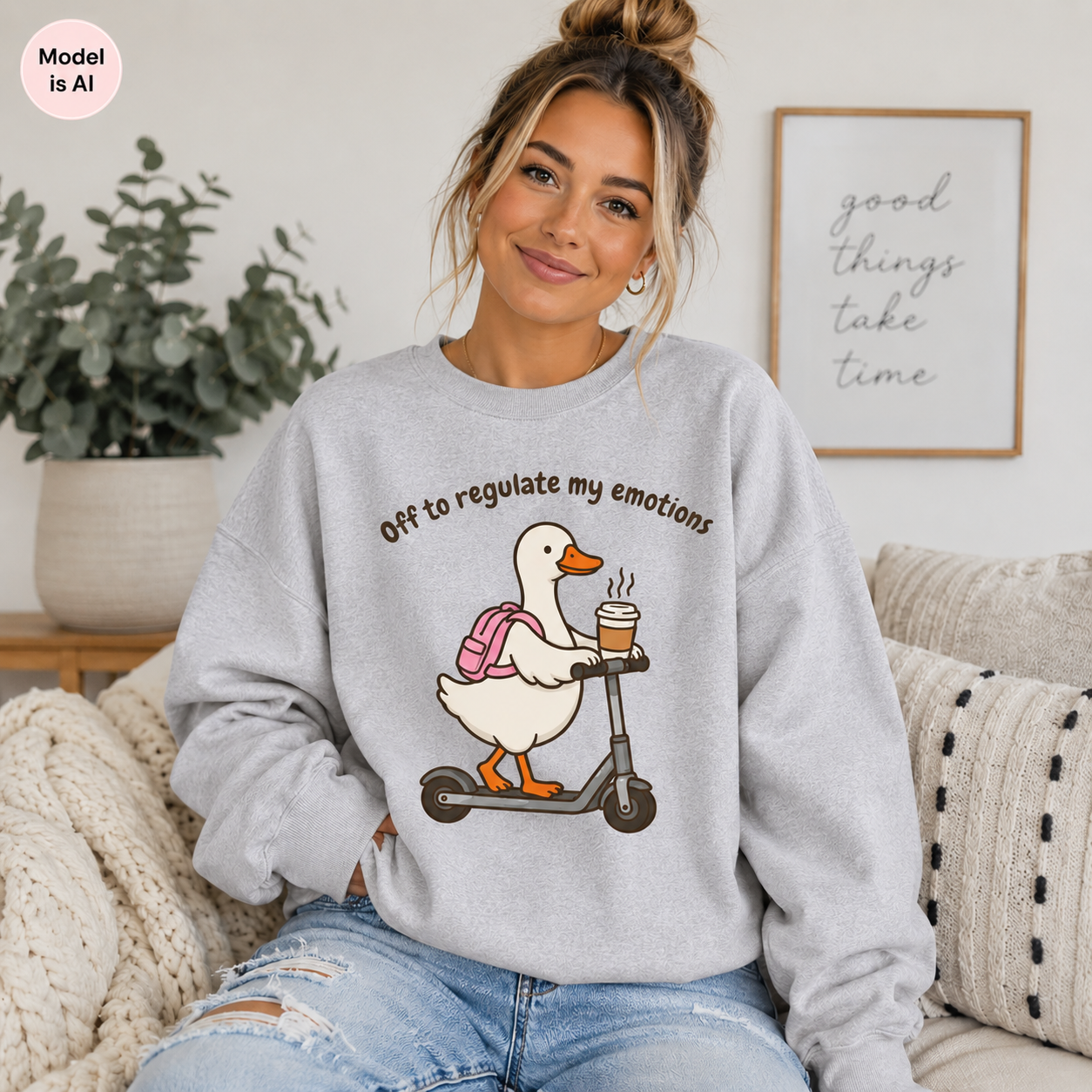 A woman sitting on a couch wearing a light gray sweatshirt with a cartoon duck on a scooter holding a coffee cup, with the text 'Off to regulate my emotions.' A framed wall print and a plant are visible in the background.