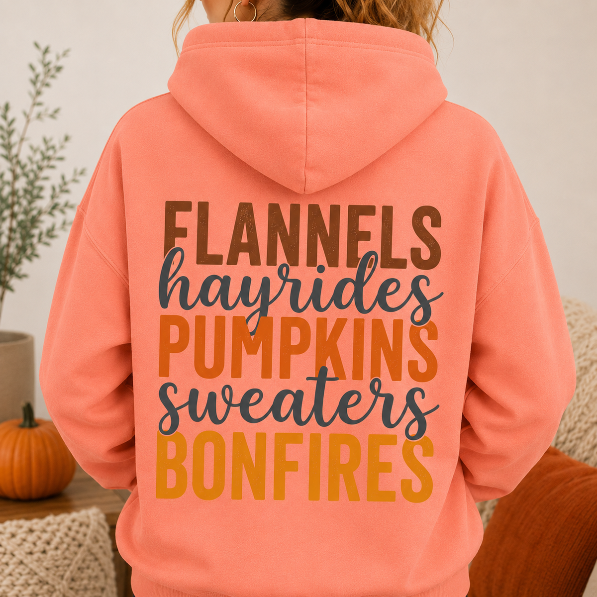 Woman wearing a Tangerine fall hoodie with Flannels, Hayrides, Pumpkins, Sweaters and Bonfires graphic printed on the back.
