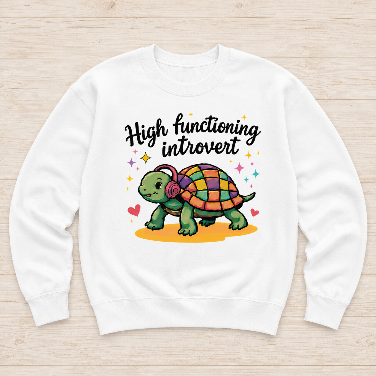 A white crewneck sweatshirt laid flat on a light wood background, featuring a colorful graphic of a cartoon turtle wearing headphones with the text 'High functioning introvert' above it.
