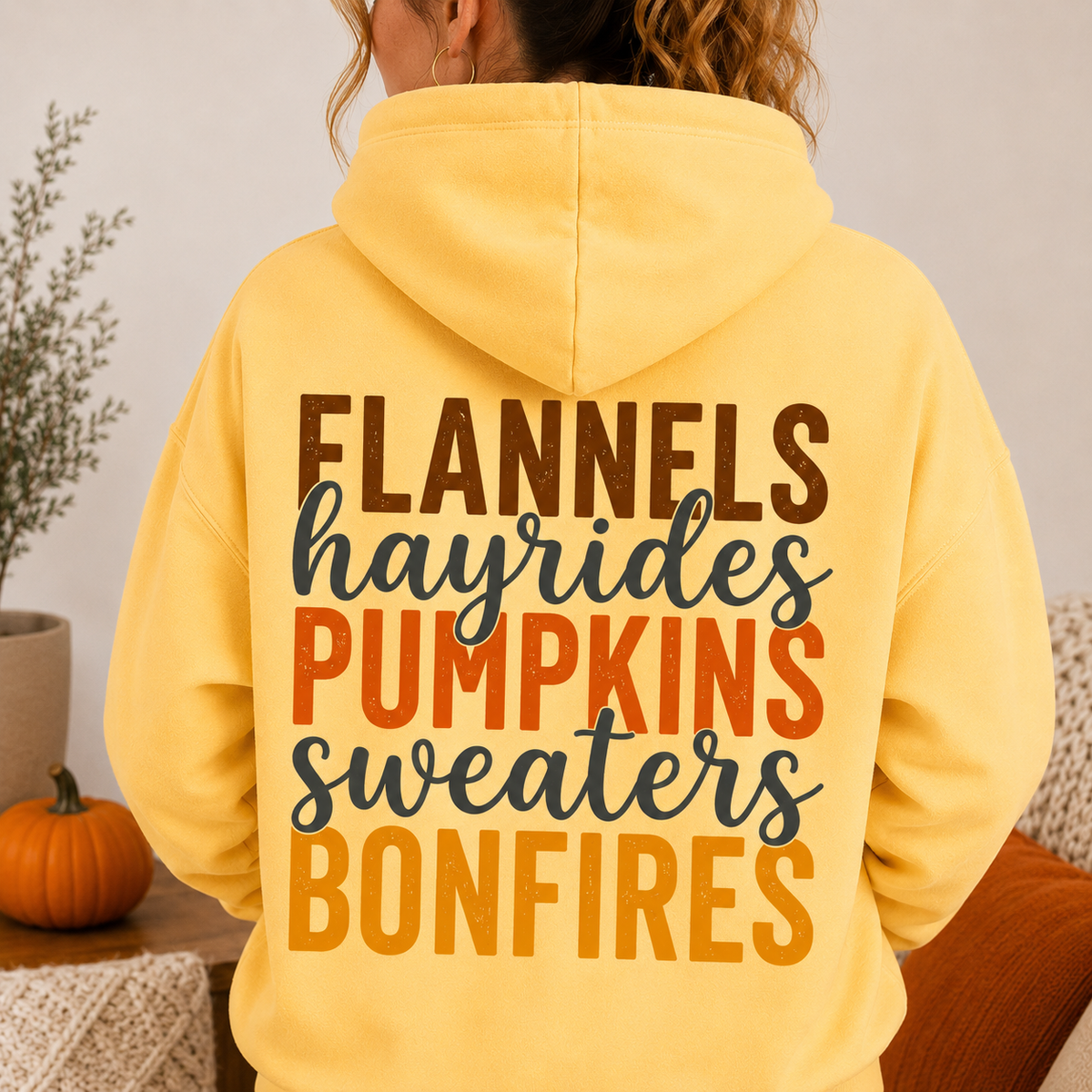 Woman wearing a Yellow Haze fall hoodie with Flannels, Hayrides, Pumpkins, Sweaters and Bonfires graphic printed on the back.